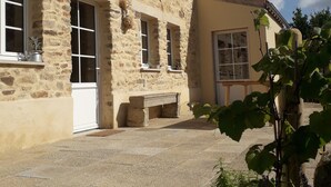 Un edificio de piedra con varias ventanas y una puerta, un banco afuera, y un cielo despejado.
