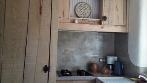 Una cocina compacta con armarios de madera, cocina a gas, cafetera y un lavamanos pequeño.