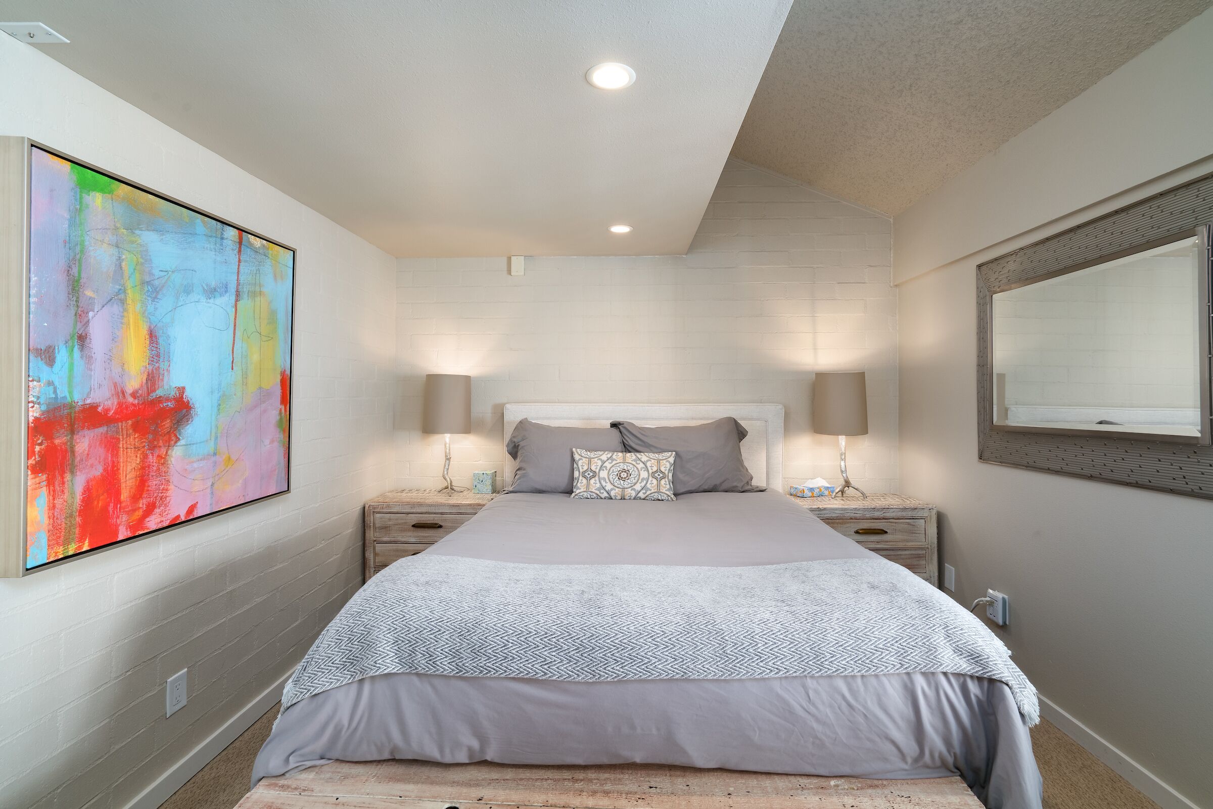 A bedroom with a large bed, two bedside tables, a nightstand, a wall-mounted TV, and a ceiling light.