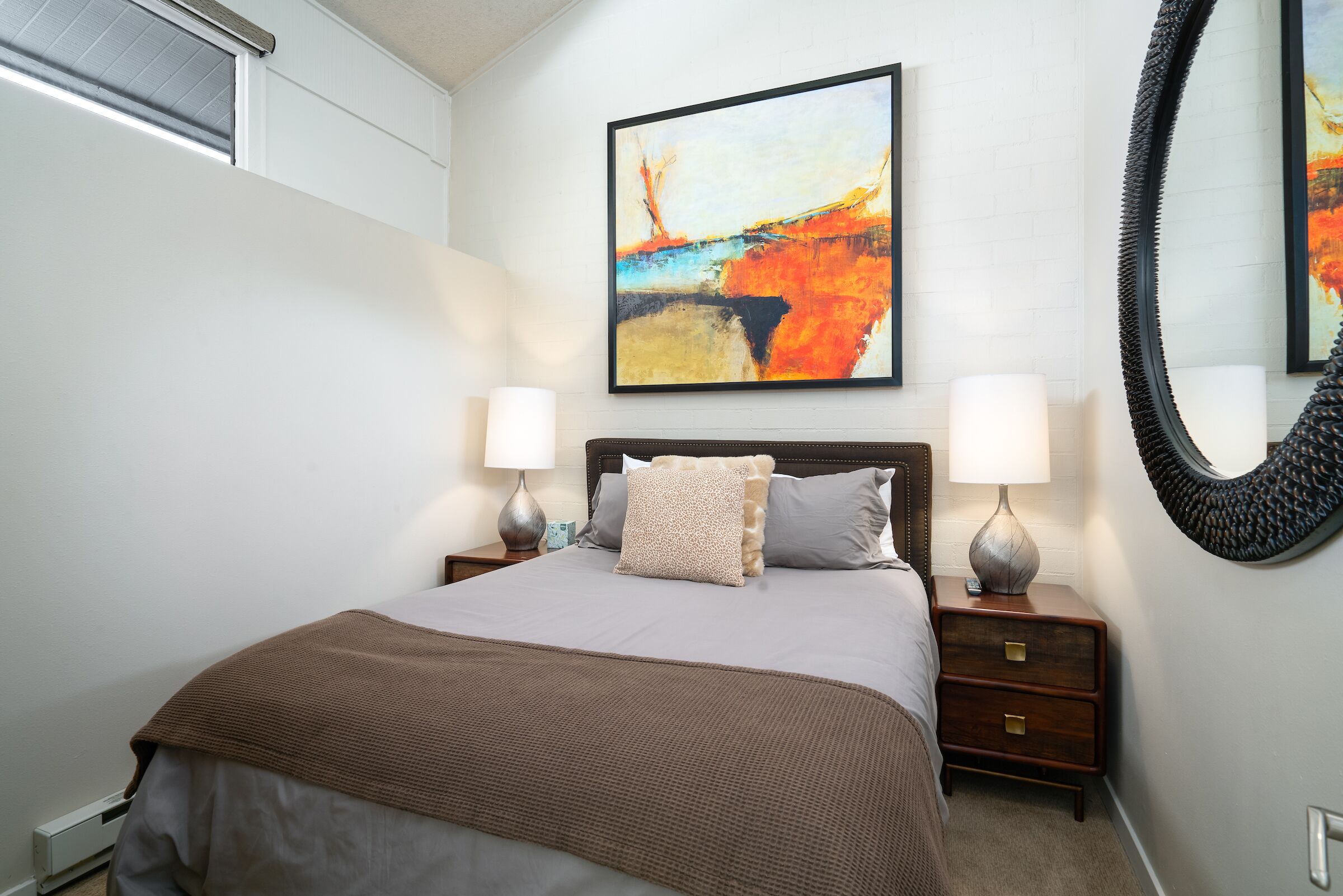 Un dormitorio con cama, dos mesitas de noche, un espejo grande y un cuadro en la pared.