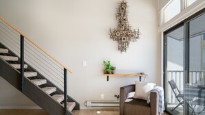 Un intérieur moderne avec un escalier, un élément décoratif fixé au mur, une petite étagère avec une plante, et un coin salon confortable avec un canapé et un fauteuil.