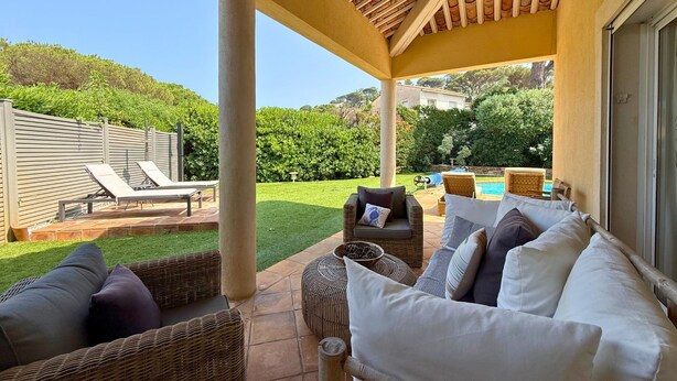 Un patio cubierto con muebles de mimbre, una piscina y un césped cuidado.