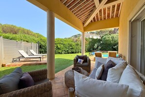 A covered patio with wicker furniture, a pool, and a well-maintained lawn.