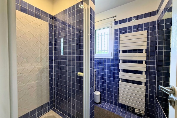 A bathroom with blue tiles, a shower, a toilet, and a window.