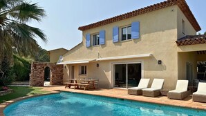 Una casa de dos pisos con piscina, un patio con mesa y sillas, y un arco de piedra.