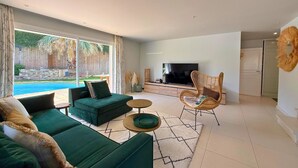 Un salón moderno con un sofá verde, televisor y vista a la piscina.