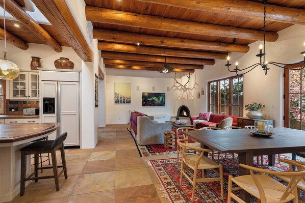 A spacious kitchen with a dining area, wooden ceiling beams, and a fireplace. - Spacious, Historic Downtown Jewel, Walk Everywhere (Santa Fe)