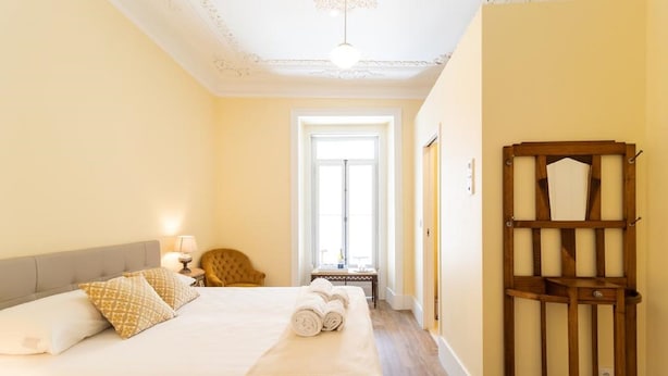 Hotellihuone, jossa on suuri sänky, yöpöytä lampun kanssa, tuoli ja puinen kaappi.