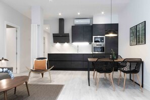 Une cuisine moderne avec des meubles de rangement aux couleurs sombres, un four encastré et un luminaire suspendu.