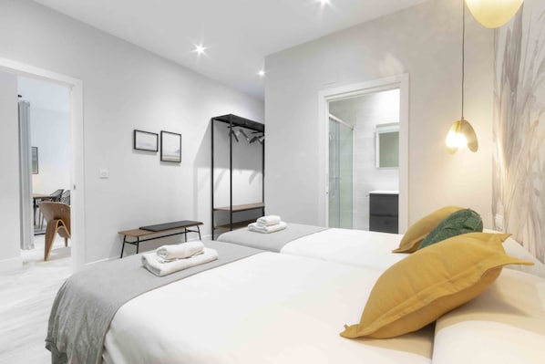 A modern hotel room with a large bed, a desk, a chair, and a shower area. - Getaria | The Rentals Collection (San Sebastián/Donostia)