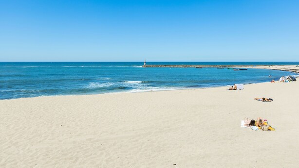 Ein weiter Sandstrand mit blauem Himmel und ruhiger See.
