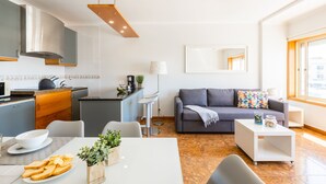 Ein modernes Wohnzimmer mit grauem Sofa, einem Couchtisch und einem Essbereich mit weißem Tisch und Stühlen.