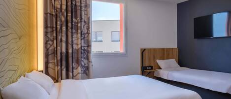 Una habitación de hotel con una cama grande, dos camas más pequeñas, un televisor y una ventana con cortinas.
