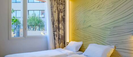 A hotel room with two beds, a window with curtains, and a wall with a textured design.