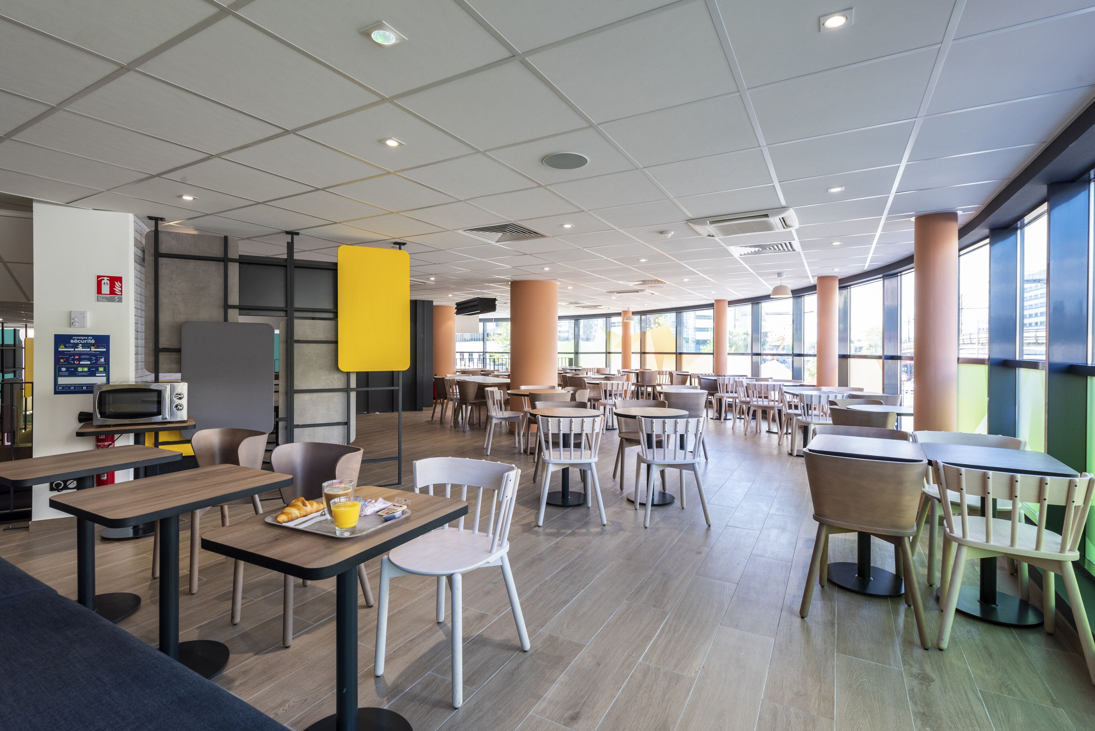 Eine großzügige Cafeteria mit mehreren Tischen und Stühlen, einer Mikrowelle und einem Automaten.