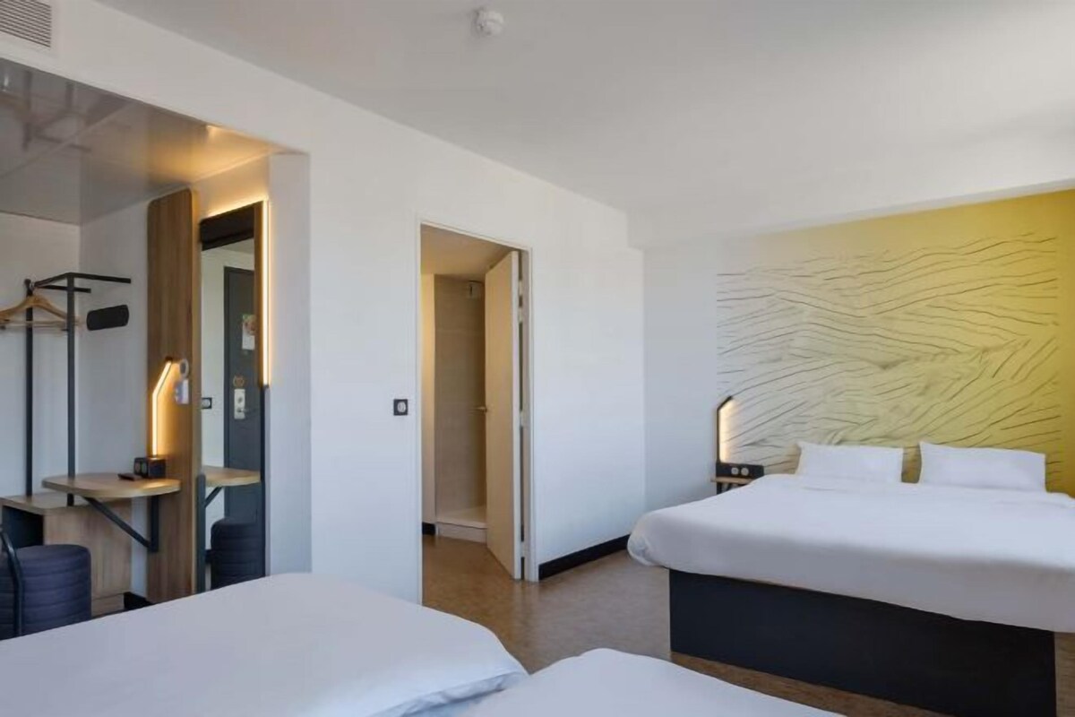A hotel room with two beds, a desk, a wardrobe, and a mirror.
