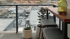 Un balcó amb vista a un paisatge urbà, una taula amb cadires i plantes en testos.