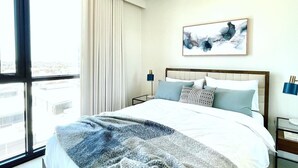 Habitació d'hotel moderna amb un llit gran, vista a la ciutat i un quadre a la paret.