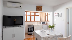 A compact kitchen with a TV, microwave, oven, and dining table with chairs. - Guest House Vulic (Dubrovnik)
