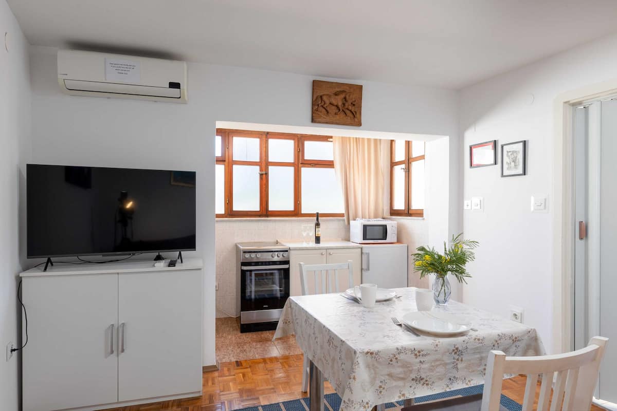 Cocina compacta con televisor, microondas, horno y mesa de comedor con sillas.