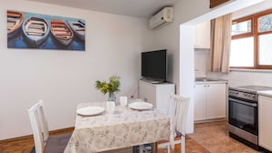 A dining area with a table set for two, a vase with flowers, and a painting of boats on the wall. - Guest House Vulic (Dubrovnik)