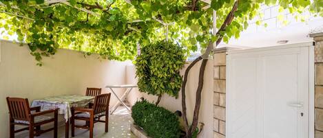 A covered patio with a table and chairs, a white door, and a small garden area.