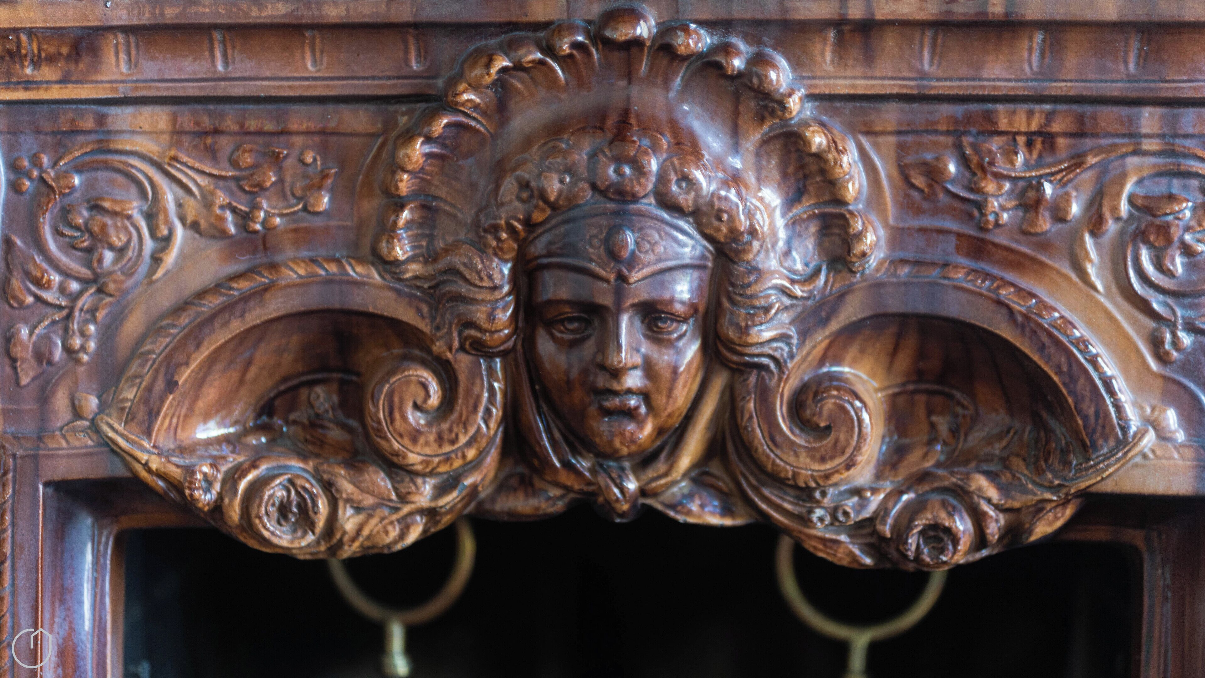Een gedetailleerd houten beeldhouwwerk met een centraal geplaatst gezicht, omringd door decoratieve versieringen.