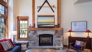Una sala de estar acogedora con chimenea de piedra, un ventanal grande y una viga de madera en el techo.