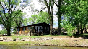 A cabin by a river with a stone foundation, wooden deck, and a hammock. - River House on the River (Gunnison)