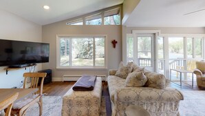 A spacious living room with a large flat-screen TV, a wooden dining table, and a sofa with patterned cushions. - River House on the River (Gunnison)