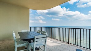 A balcony with a table and chairs, a view of the sea, and a clear sky. - Phoenix West beachfront 3BR/4BA with Lazy River/Slide (Orange Beach)