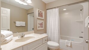 A bathroom with a double sink, a toilet, a shower with a glass door, and a mirror with two framed pictures. - Phoenix West beachfront 3BR/4BA with Lazy River/Slide (Orange Beach)