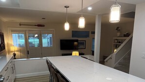 A modern kitchen with a large island, bar stools, pendant lighting, and a view of the living area.