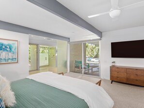 Quarto com cama, penteadeira, televisão e porta de vidro deslizante para um pátio.