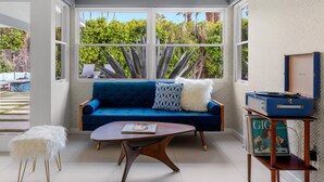 A room with a blue sofa, a white fluffy stool, a wooden coffee table, and a ceiling light fixture. - Marcia! Marcia! Marcia! – Mid-Mod PS Retreat (Palm Springs)