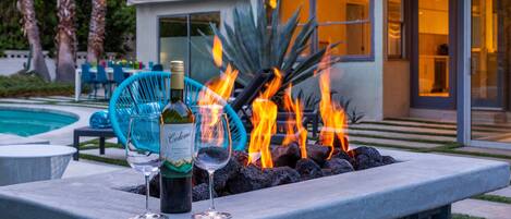 A modern outdoor seating area with a fire feature, a bottle of wine, and glasses.