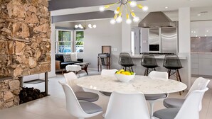 A modern kitchen with a stone accent wall, a dining area with a marble table and white chairs, and a kitchen island with bar stools. - Marcia! Marcia! Marcia! – Mid-Mod PS Retreat (Palm Springs)