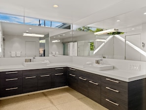 A modern bathroom with a large mirror, two sinks, dark cabinetry, and a skylight.