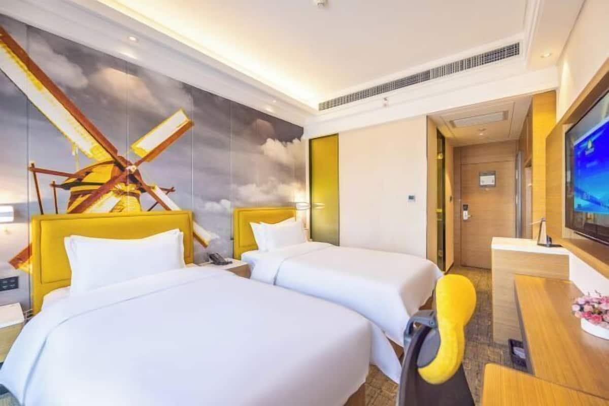 A hotel room with two beds, a desk, a television, and a mural on the wall.