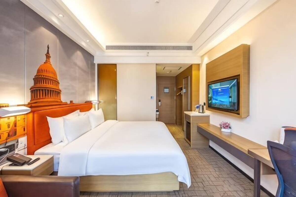 A hotel room with a large bed, a desk, a TV, and a wall with a Capitol building mural.