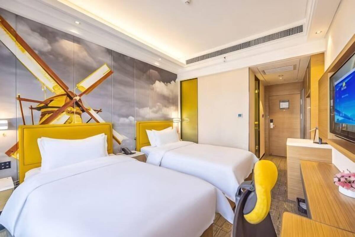A hotel room with two beds, a desk, a television, and a large window.