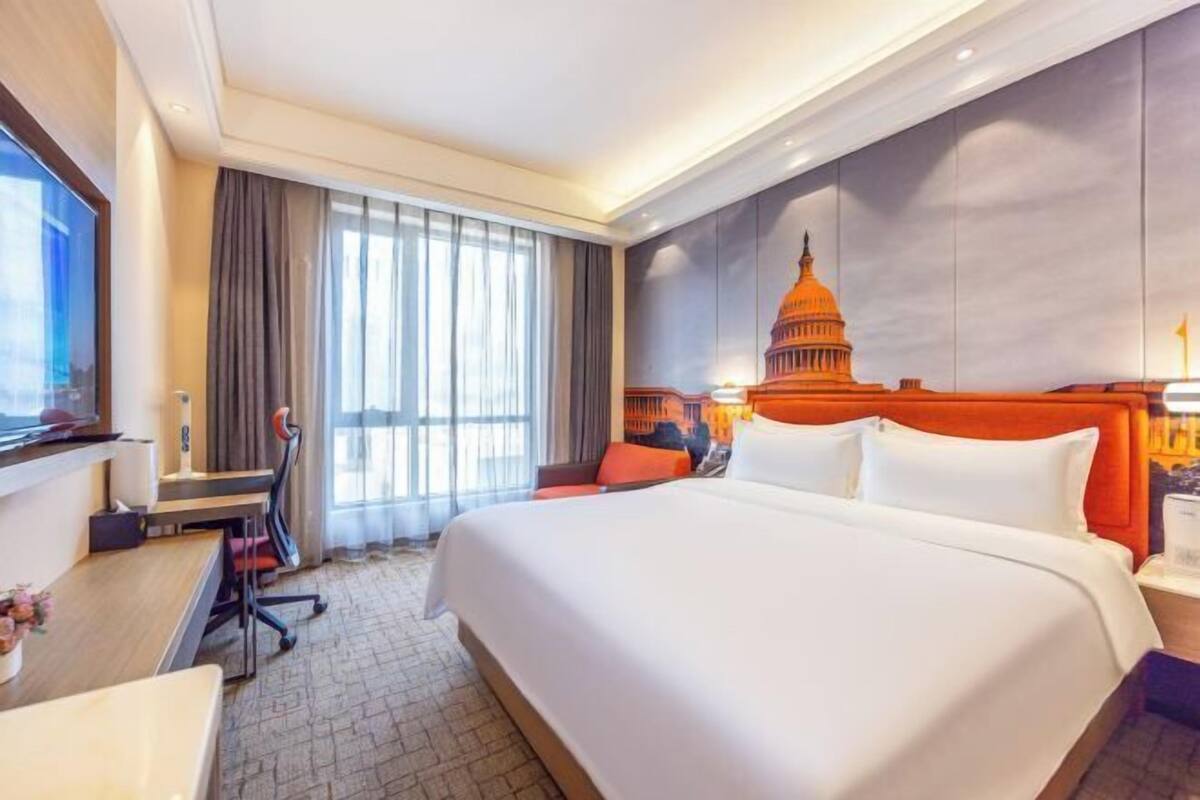 A hotel room with a large bed, a desk, a chair, a TV, and a view of the Capitol building.
