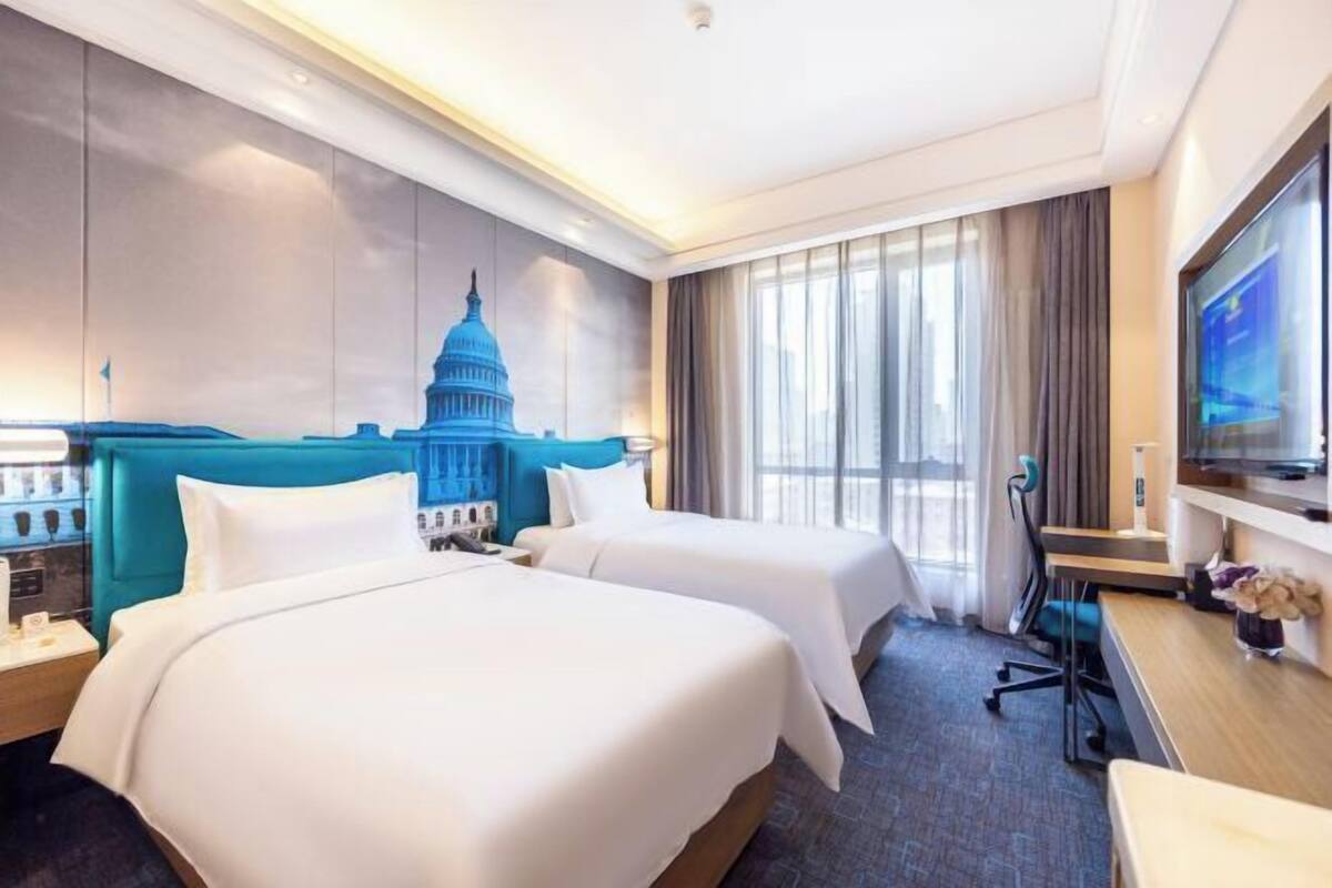 A hotel room with two beds, a desk, a TV, and a mural of a capitol building.