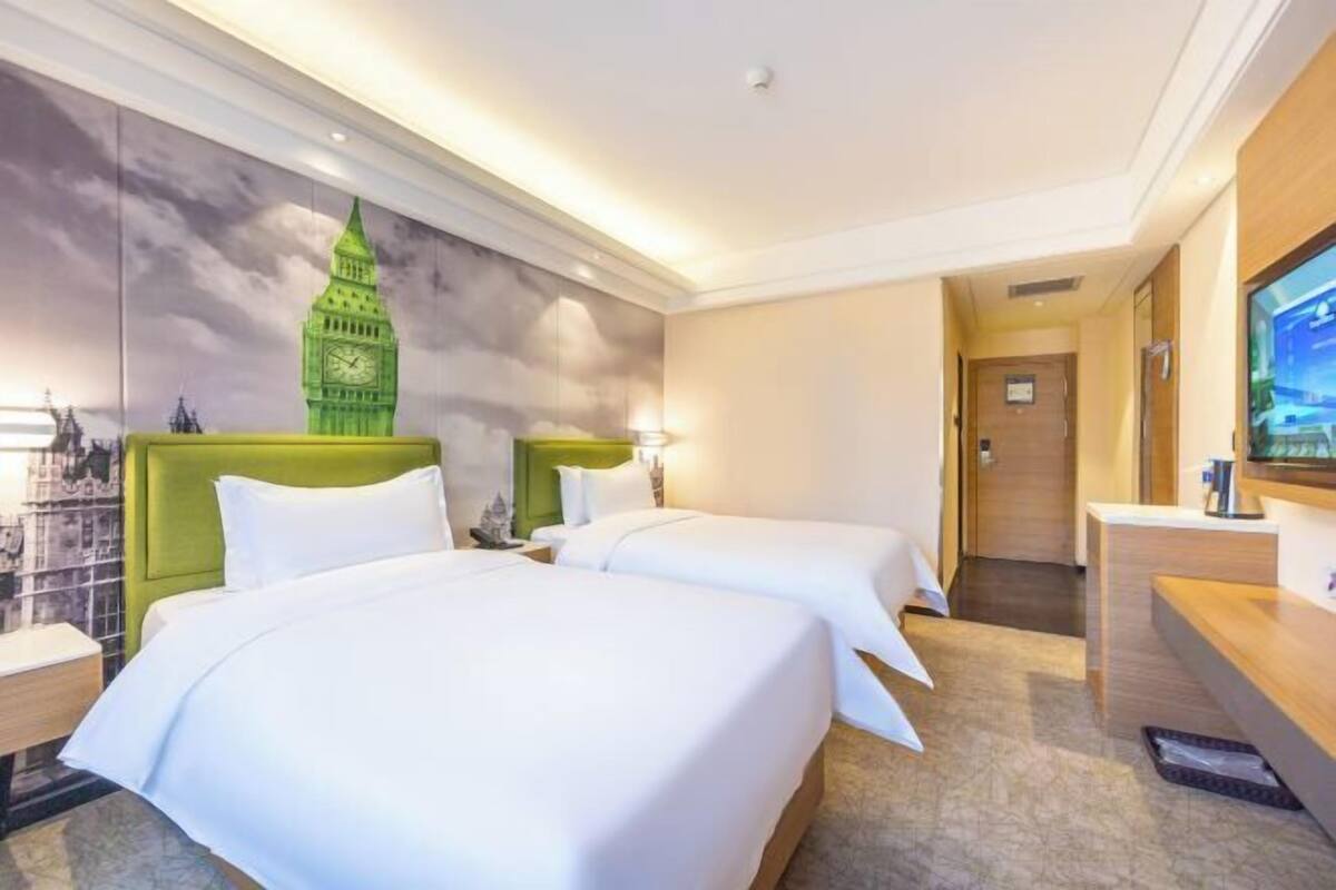 A hotel room with two beds, a green headboard, a large wall mural, a television, and a reception desk.