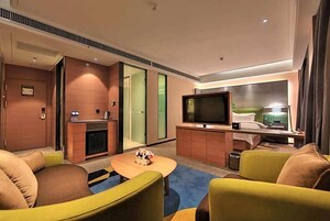 A modern hotel room with a flat-screen TV, a sofa, a coffee table, and a small kitchenette.