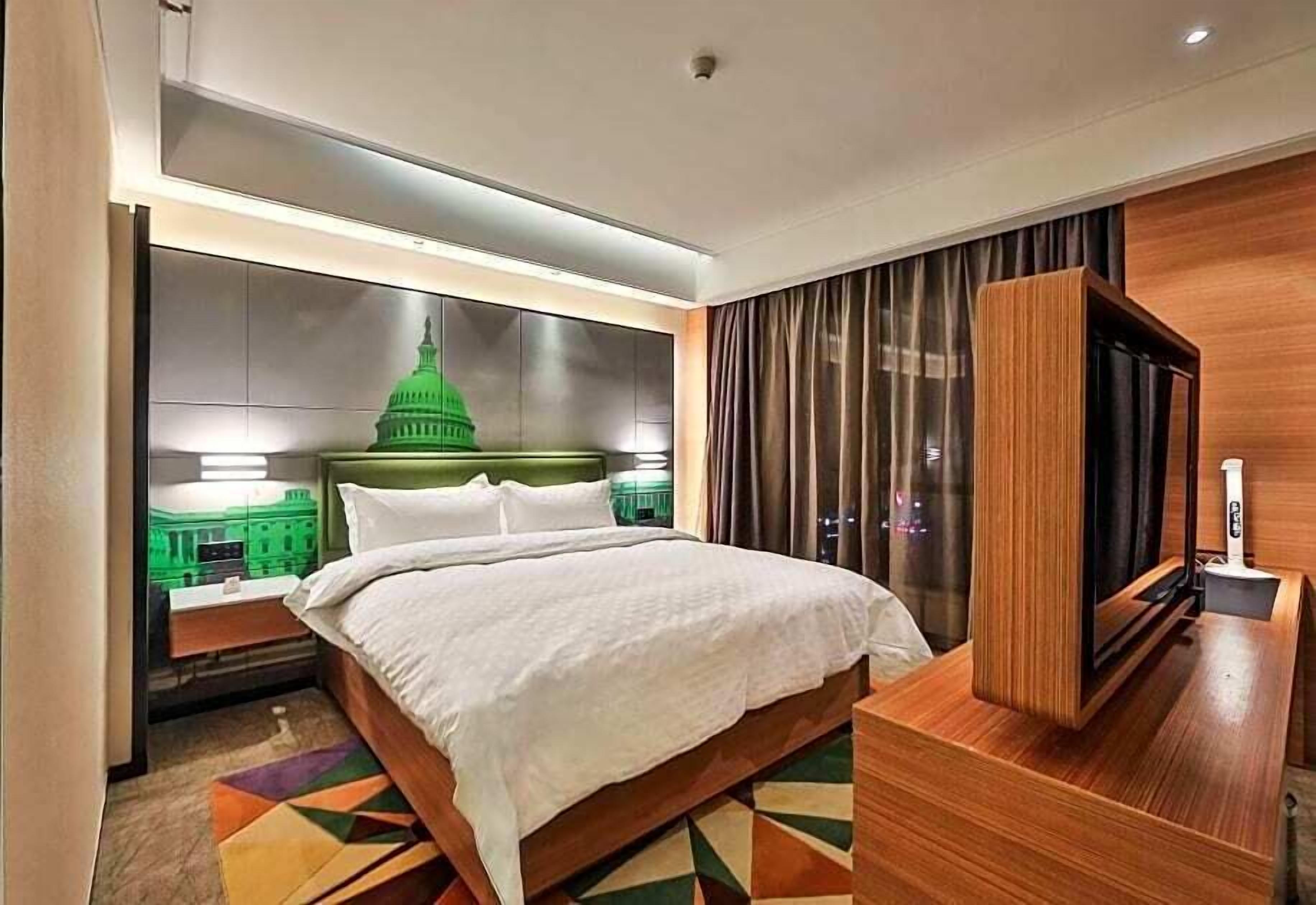 Habitación de hotel con una cama grande, televisión y vista a un edificio verde.