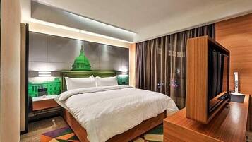 A hotel room with a large bed, a TV, and a view of a green building.