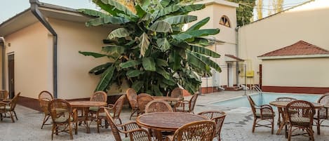 An outdoor patio with hexagonal tiled flooring, wicker furniture, and a large banana plant.