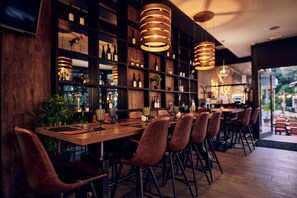 A restaurant interior with wooden tables, leather chairs, hanging pendant lights, and shelves stocked with bottles and glasses. - Paris (Opatija)