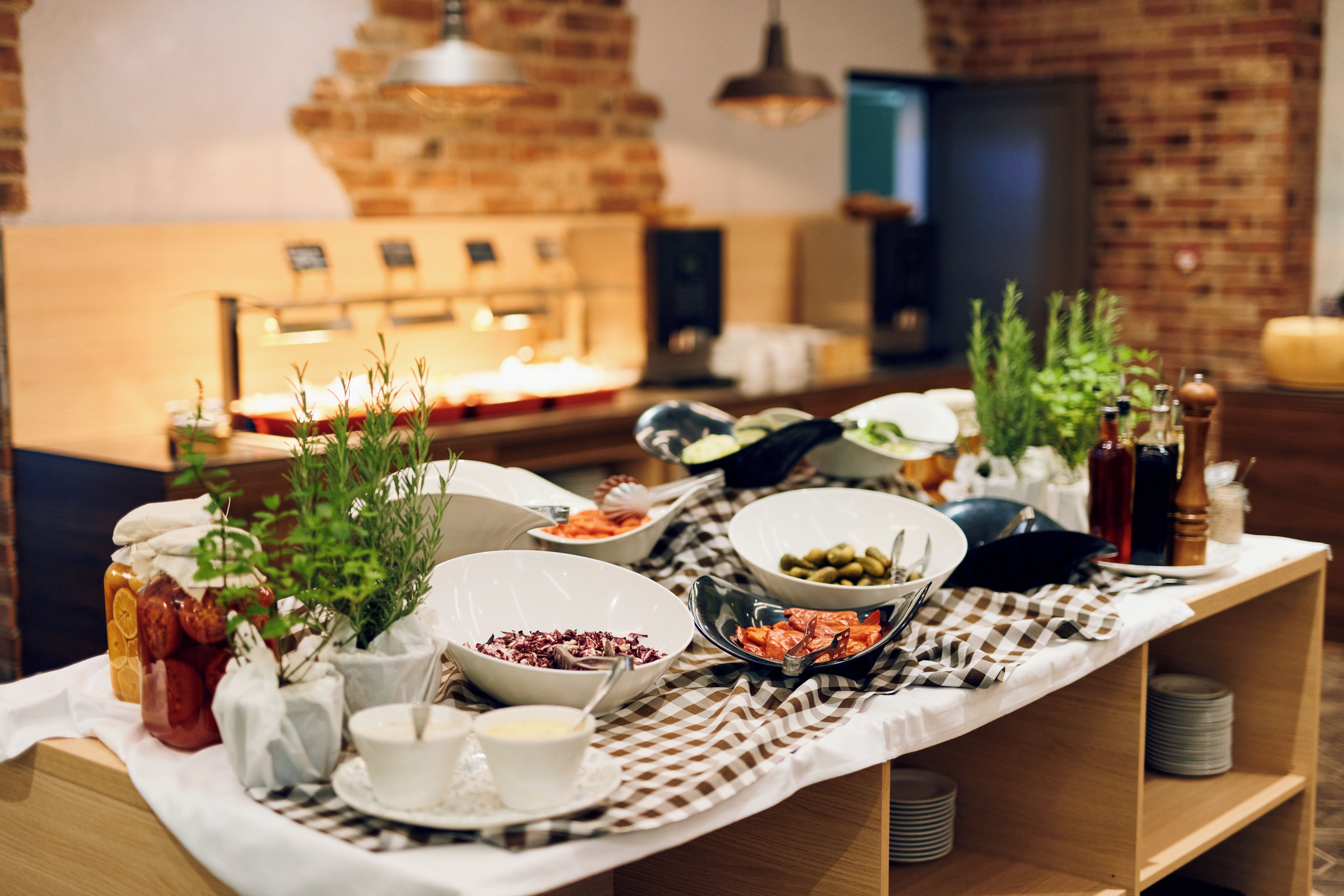 Uma mesa de buffet com diversos pratos, um espaço para café e um fundo com parede de tijolos.